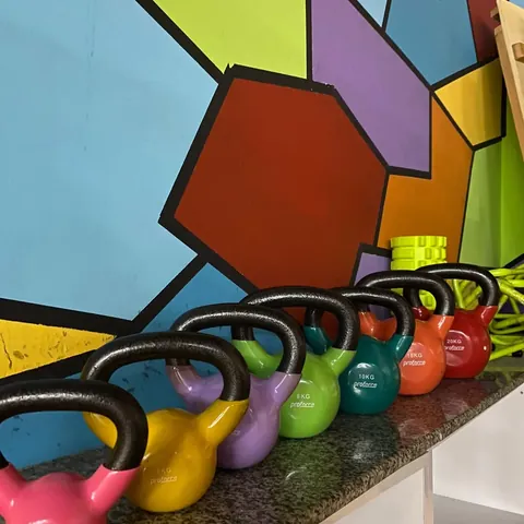 Ağırlıklarına göre dizilmiş renkli kettlebell sırası, arkada mozaik duvar